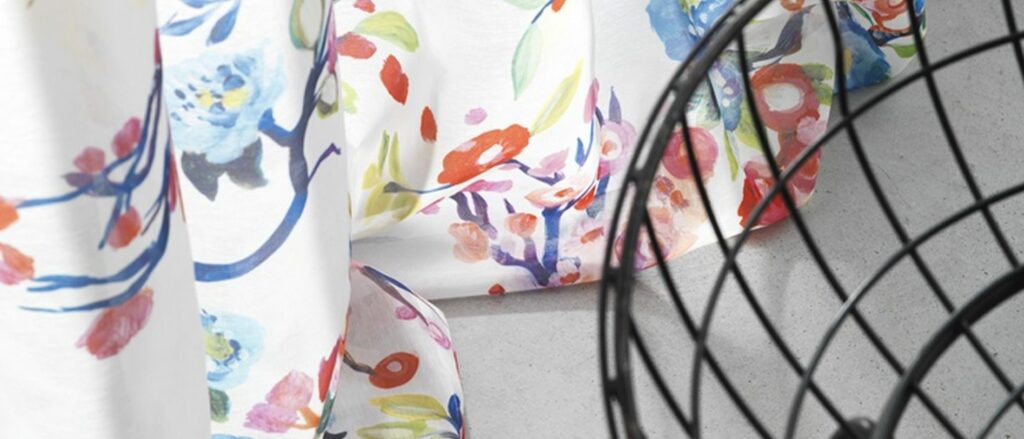 Bunte florale Gardinen mit einem Hauch von einem schwarzen Drahtkorb im Vordergrund. Firmenadresse