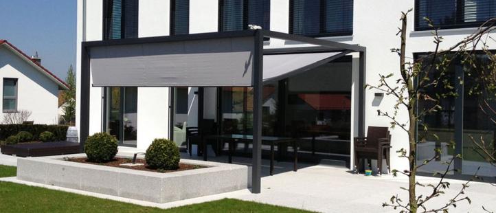 Ein modernes Haus mit überdachter Terrasse mit einziehbarer Markise, Sitzgelegenheiten im Freien und angelegtem Garten mit gestutzten Büschen präsentiert hochwertige Produkte für stilvolles Leben im Freien. - Firmenadresse